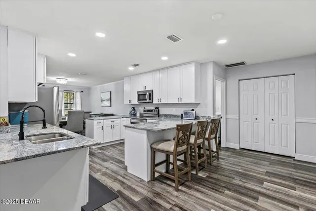 a kitchen with stainless steel appliances granite countertop a sink a stove a refrigerator cabinets and chairs