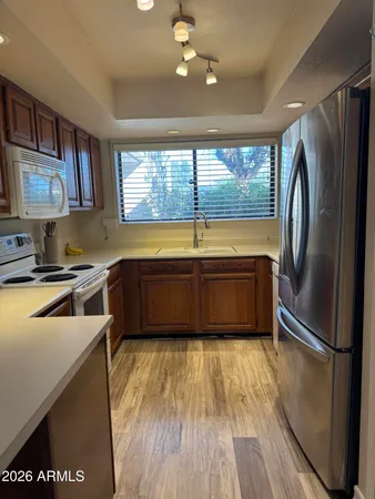 a kitchen with stainless steel appliances granite countertop a refrigerator a sink dishwasher a stove and white countertops with wooden floor