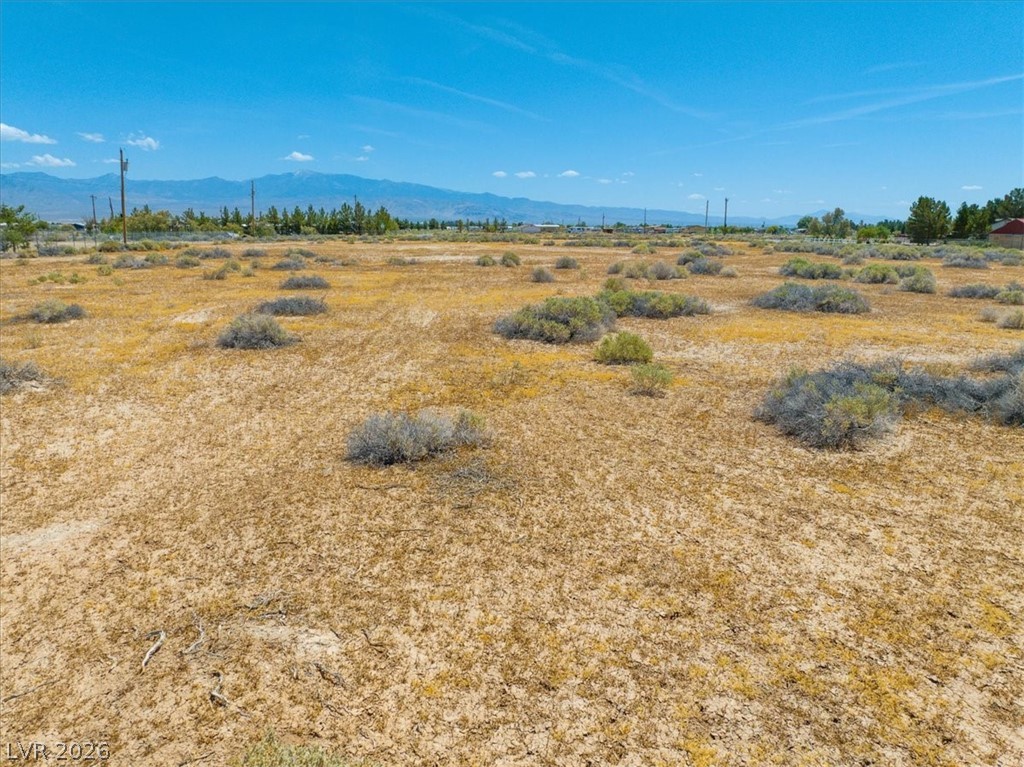 4610 Lawrence Road Pahrump, NV 89048 - Photo 9 of 42 A vast, undeveloped parcel of land awaits, framed by distant mountains and a bright sky.