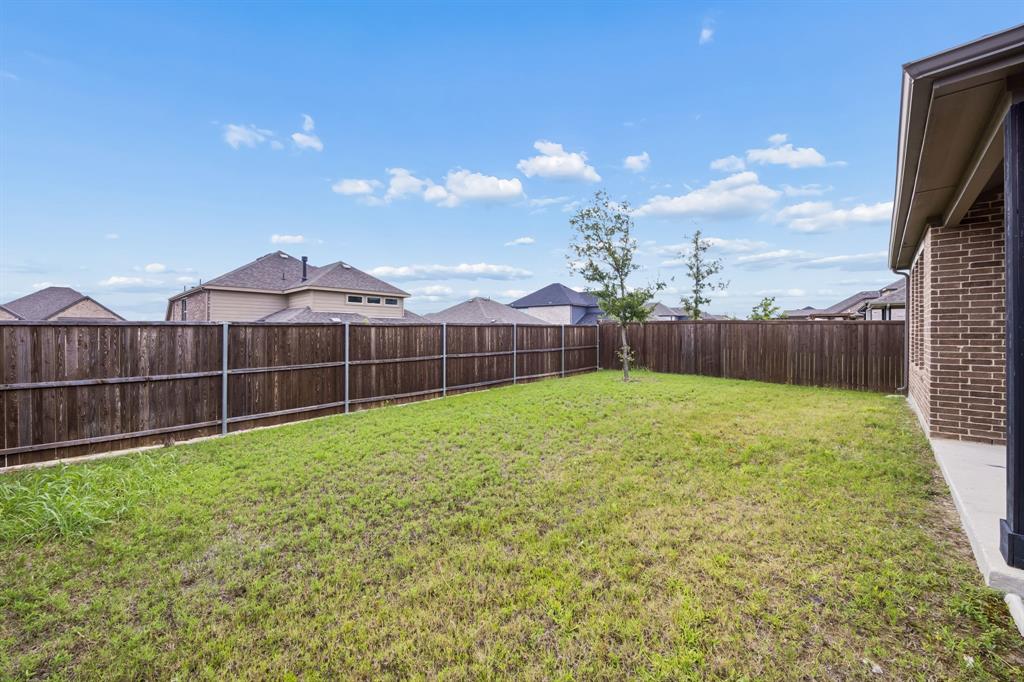 1303 Wheelwright Drive Forney, TX 75126 - Photo 35 of 39 Expansive backyard with a wooden privacy fence, a young tree, and a partial brick exterior