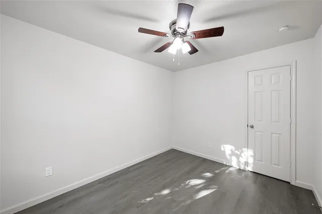 an empty room with wooden floor ceiling fan and window