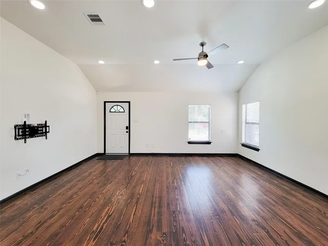an empty room with wooden floor chandelier fan and windows