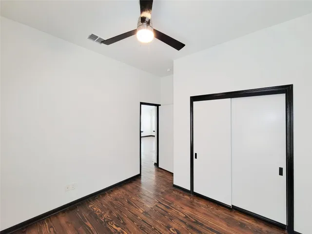 a view of an empty room with wooden floor and a ceiling fan