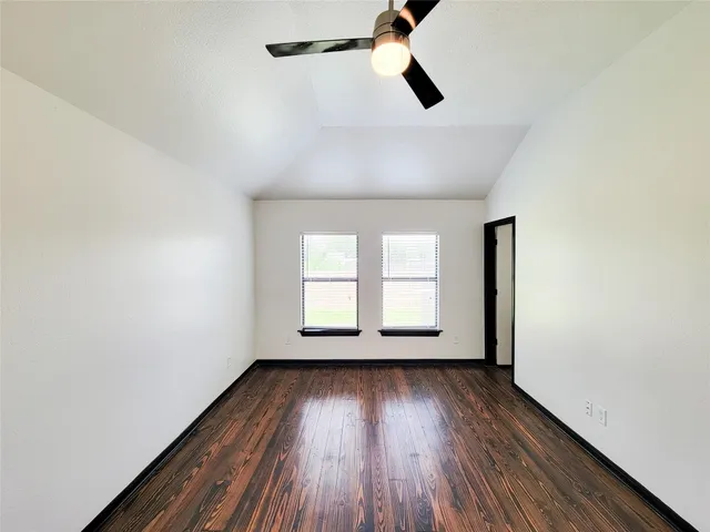 an empty room with wooden floor fan and windows