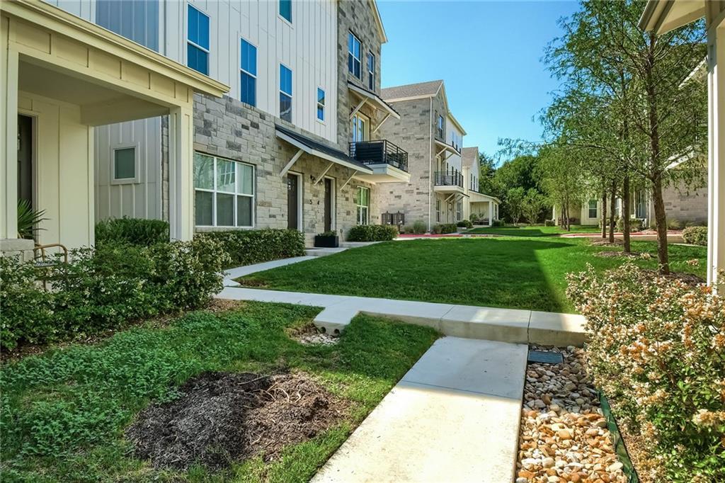 2624 Metcalfe Road, Unit 7 Austin, TX 78741 - Photo 3 of 31 Stone and siding exteriors featuring multiple windows, a second-story balcony, covered entryway, and a lush lawn bordered by mature trees and shrubs