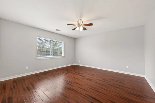 an empty room with wooden floor ceiling fan and windows