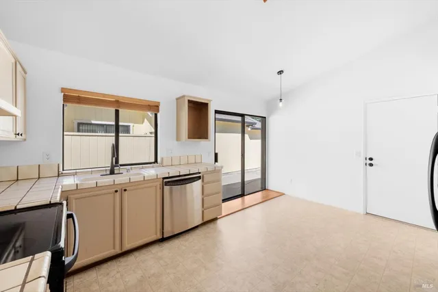 a large white kitchen with granite countertop a sink and white cabinets next to a window