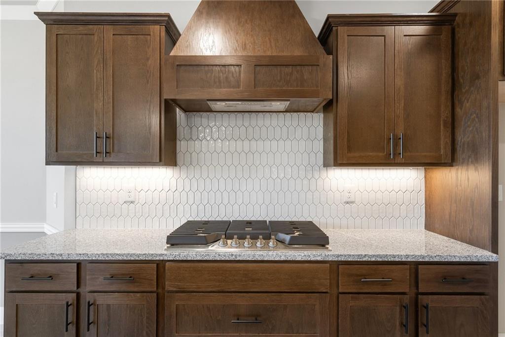 1910 Peacock Road Centerton, AR 72719 - Photo 7 of 29 Custom range hood above a gas cooktop, quartz-finish countertop, dark wood-finish cabinetry, and white geometric tile backsplash
