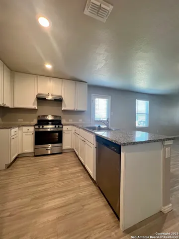 a large kitchen with granite countertop a stove top oven a sink dishwasher and white cabinets with wooden floor