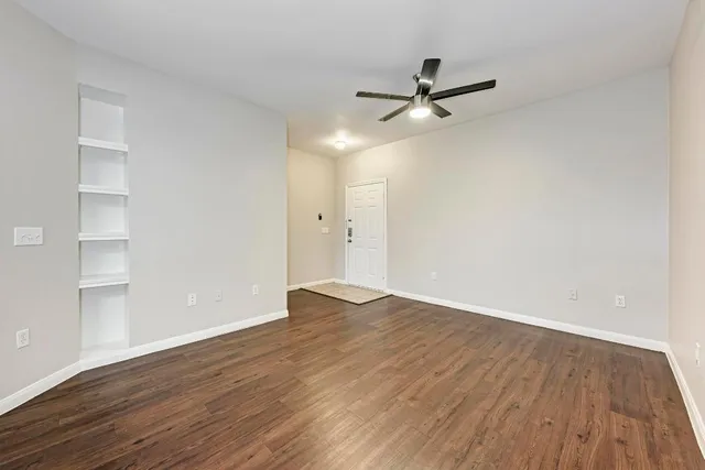 an empty room with wooden floor a ceiling fan and windows