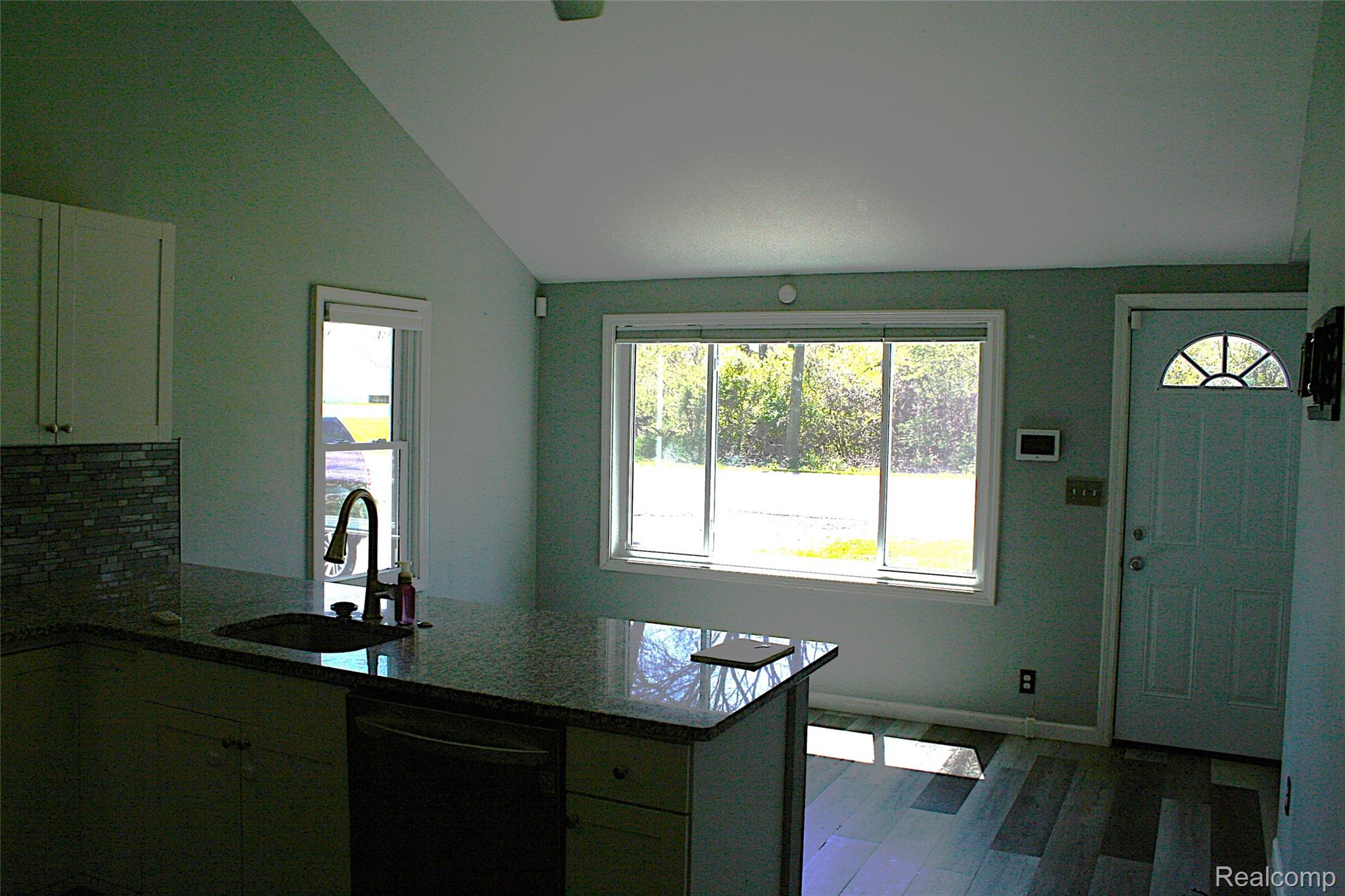Kitchen with dark stone countertops, a peninsula, dishwashing machine, dark wood-style floors, and lofted ceiling