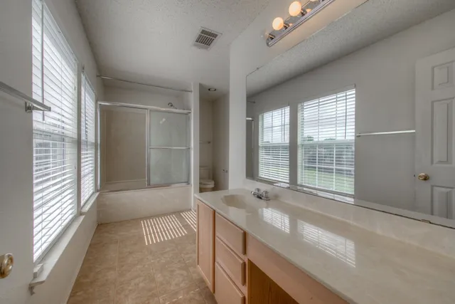 a bathroom with a granite countertop sink a large mirror and a bathtub next to a window
