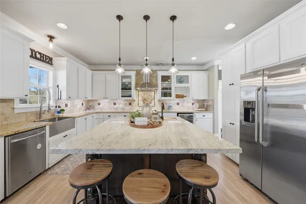 a kitchen with stainless steel appliances granite countertop a sink a stove a refrigerator and chairs