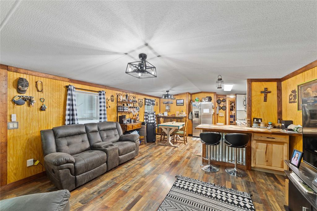 Living area with dark wood-style flooring, wooden walls, vaulted ceiling, and a textured ceiling