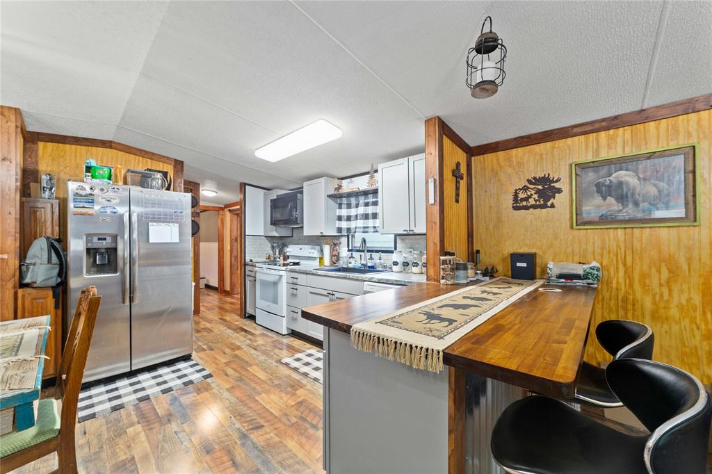 4991 Thunderbird Drive May, TX 76857 - Photo 15 of 34 Kitchen with a sink, black microwave, wood walls, white electric stove, and stainless steel fridge with ice dispenser