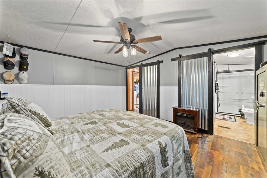 4991 Thunderbird Drive May, TX 76857 - Photo 18 of 34 Bedroom featuring hardwood / wood-style floors, a barn door, wainscoting, a ceiling fan, and lofted ceiling