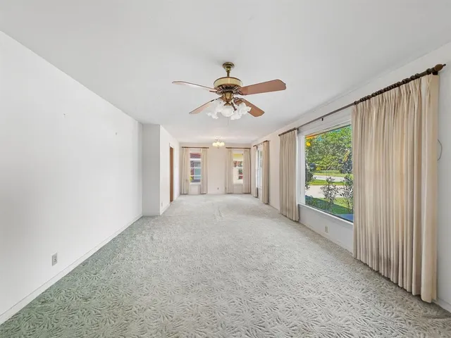 an empty room with chandelier fan and windows