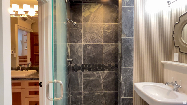 426 West Center Street Parowan, UT 84761 - Photo 51 of 107 Shower enclosure featuring large format stone-finish tile with a hexagonal mosaic accent band, a glass door with a polished chrome handle, and a wall-mounted showerhead