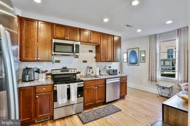 a kitchen with stainless steel appliances granite countertop wooden cabinets a sink a stove a refrigerator and grey cabinets