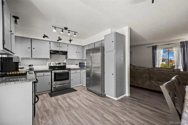 a kitchen with granite countertop a refrigerator oven a sink dishwasher and white cabinets with wooden floor