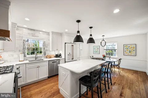 a kitchen with stainless steel appliances granite countertop a stove a refrigerator a kitchen island a dining table and chairs with wooden floor