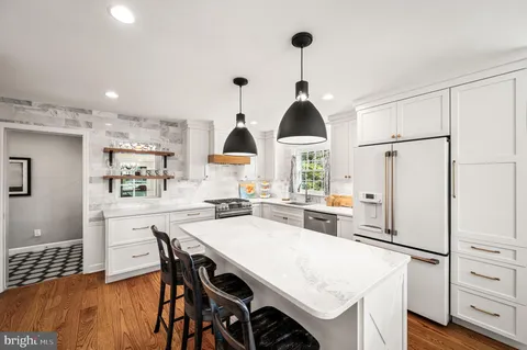a kitchen with stainless steel appliances kitchen island granite countertop a stove a refrigerator a sink a dining table and chairs with wooden floor
