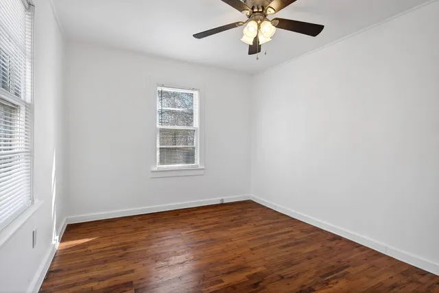 an empty room with wooden floor chandelier fan and windows