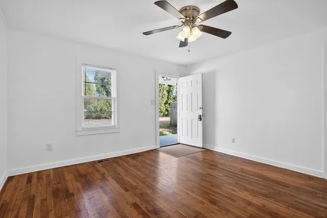 an empty room with wooden floor chandelier fan and windows