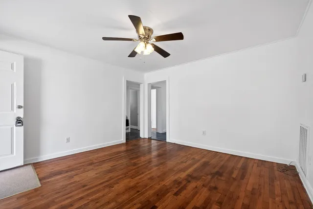 a view of an empty room with wooden floor and a ceiling fan