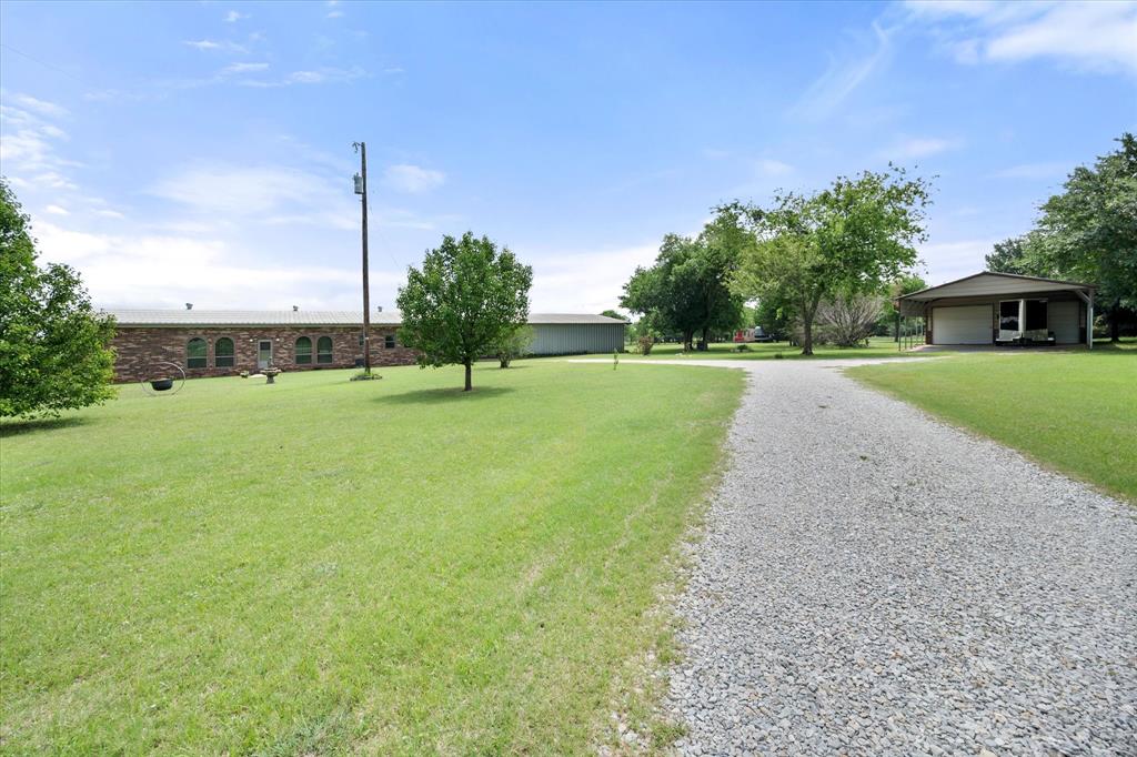 2101 Ridge View Drive Cleburne, TX 76033 - Photo 6 of 31 Expansive gravel driveway leading to a brick-front structure with arched windows, surrounded by green lawns and mature trees