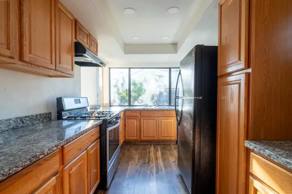 a kitchen with granite countertop a refrigerator a sink a stove and wooden cabinets