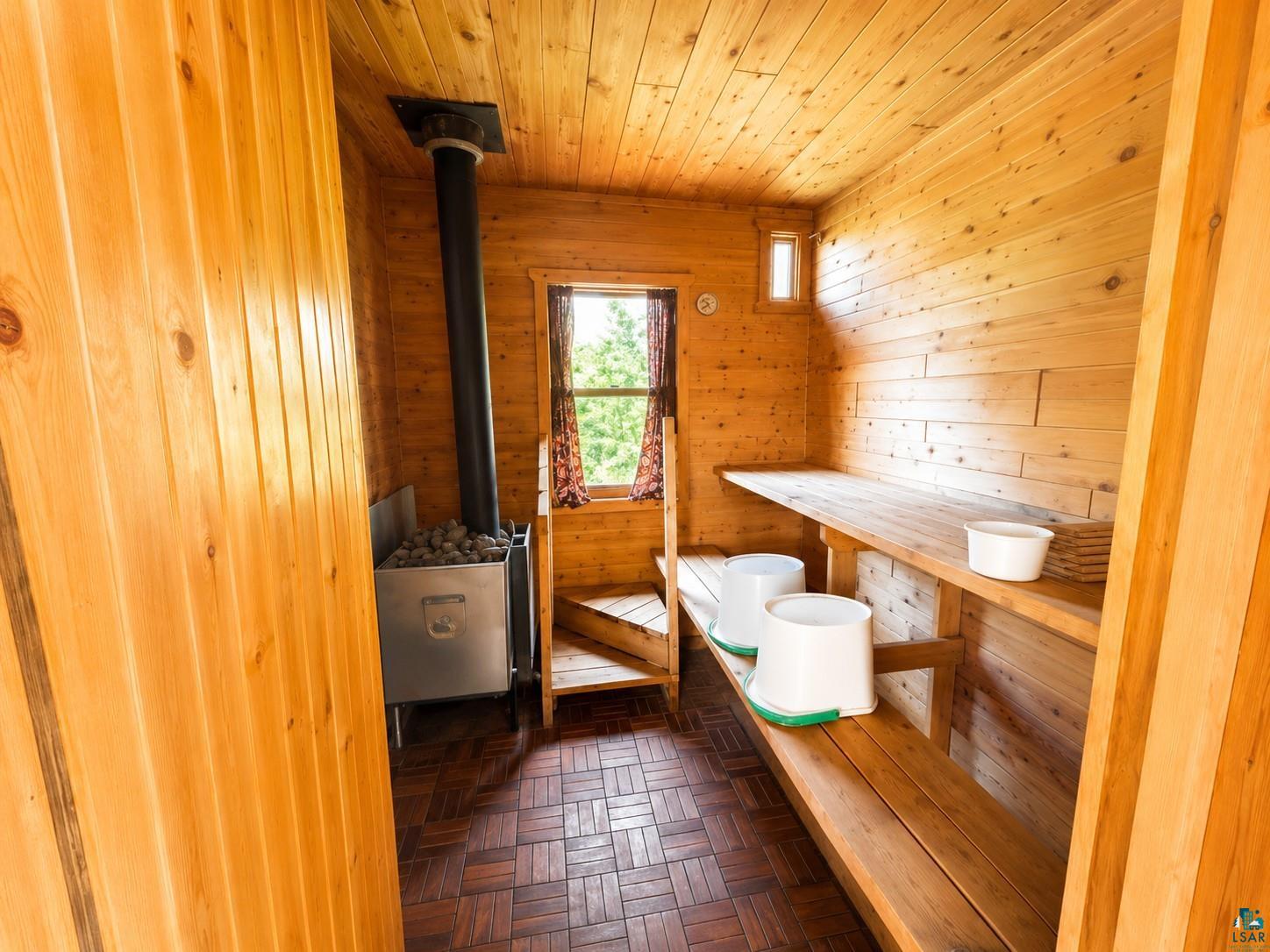 1787 North Bay Road Ely, MN 55731 - Photo 36 of 40 Wood-paneled sauna featuring a wood-burning heater with a black flue, built-in wooden benches, and a small window for natural light