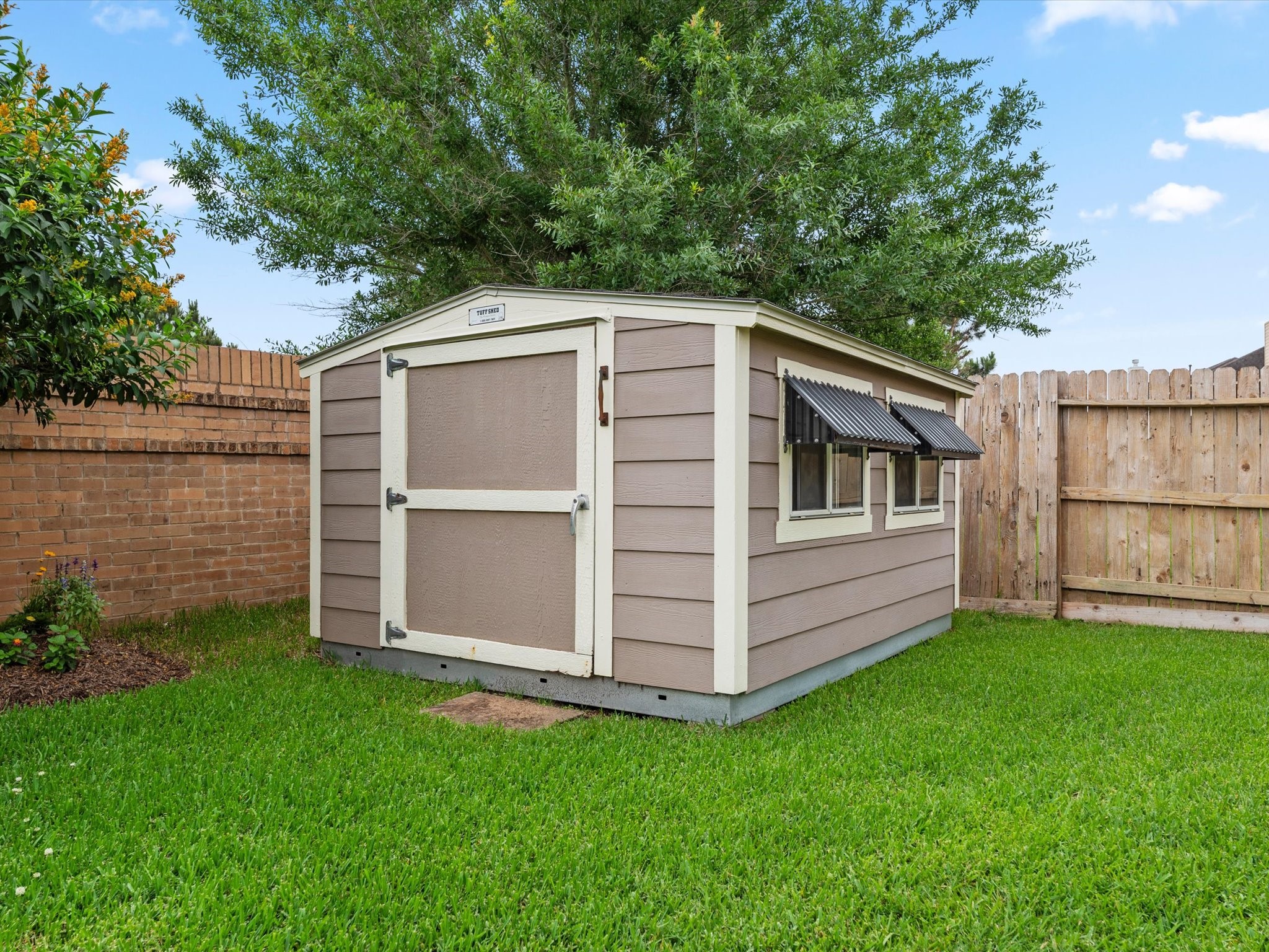 3907 Randle Ridge Court Fulshear, TX 77441 - Photo 38 of 46 This photo shows a tidy backyard with a small, well-maintained shed. The shed features a neutral exterior, windows with awnings, and is surrounded by a lush green lawn. It's enclosed by a wooden and community brick fence, offering privacy and a cozy outdoor space.