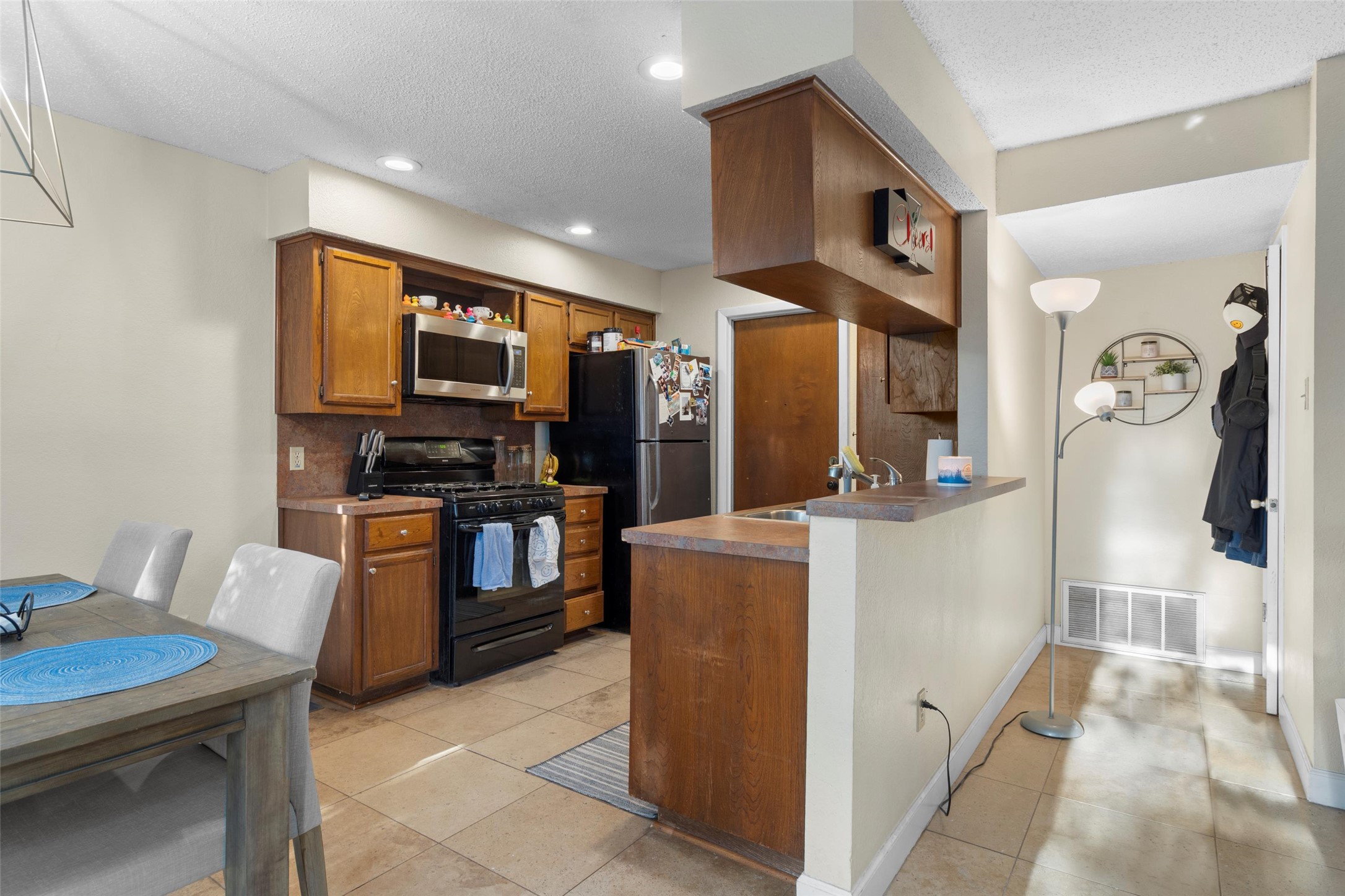 6492 Hart Lane Austin, TX 78731 - Photo 8 of 22 Kitchen featuring appliances with stainless steel finishes, brown cabinets, light tile patterned floors, open shelves, and a textured ceiling