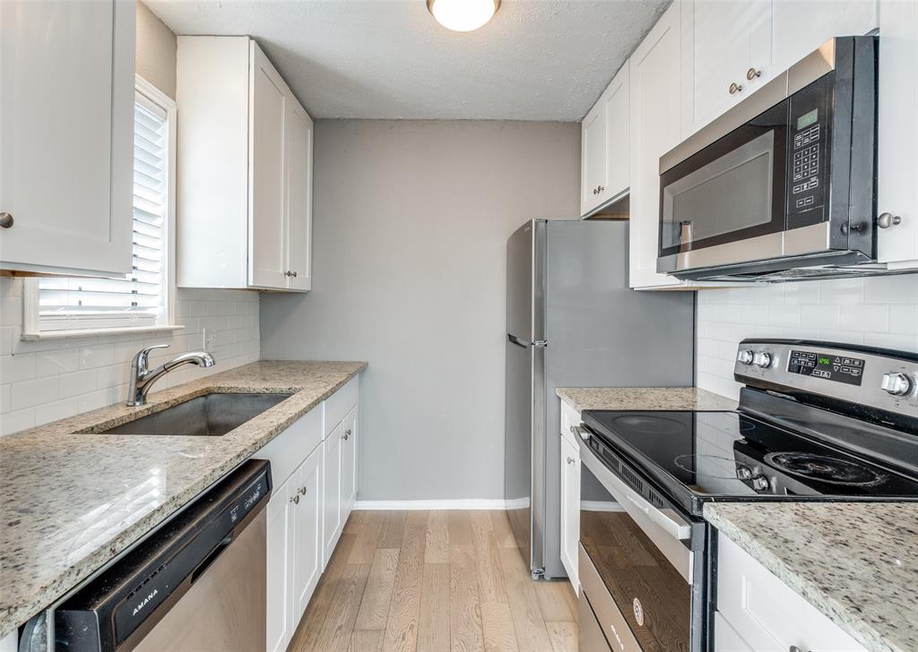 Kitchen with backsplash, appliances with stainless steel finishes, light wood finished floors, white cabinetry, and a textured ceiling