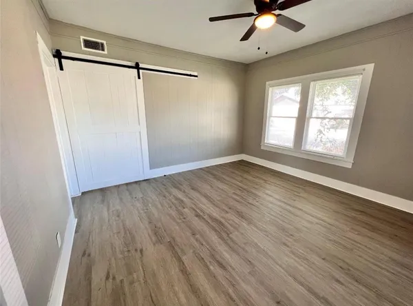 an empty room with wooden floor fan and windows