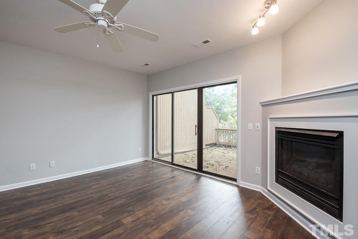 4213 Sunshadow Lane Raleigh, NC 27613 - Photo 4 of 20 an empty room with wooden floor fireplace fan and windows