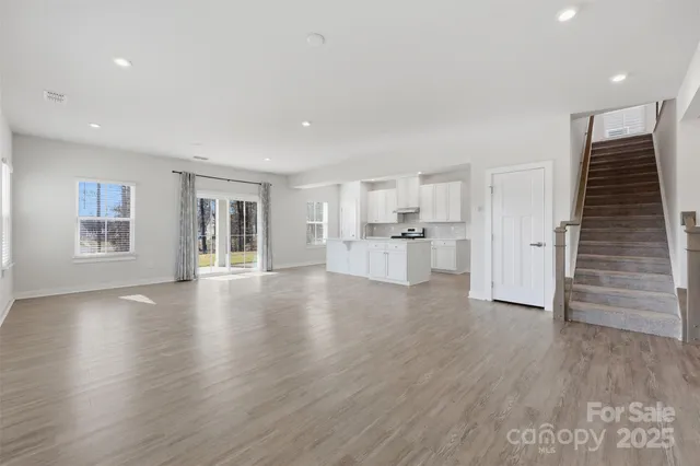 a view of empty room with wooden floor and kitchen