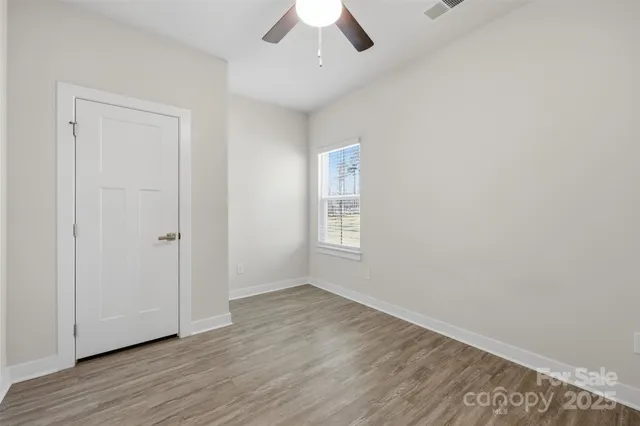 an empty room with wooden floor chandelier fan and windows