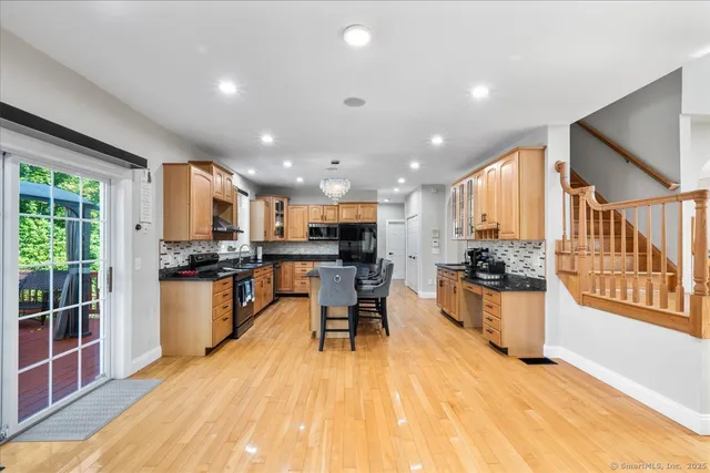 a kitchen with stainless steel appliances kitchen island granite countertop a stove top oven a sink a dining table and chairs with wooden floor