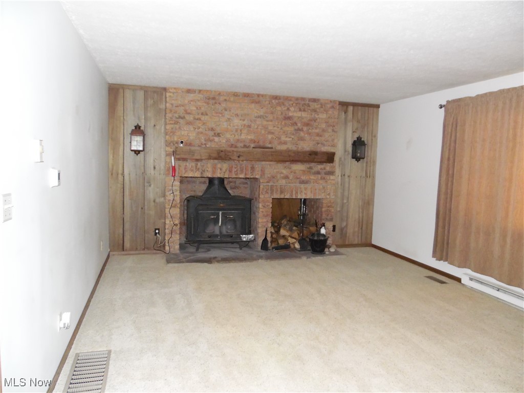 2800 Tick Ridge Road Lower Salem, OH 45745 - Photo 21 of 28 Unfurnished living room featuring carpet floors, baseboards, visible vents, and a wood stove