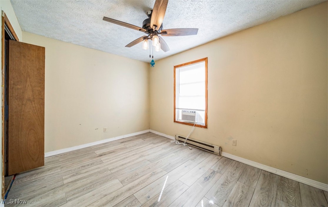 5919 North Bend Road Ashtabula, OH 44004 - Photo 23 of 24 Empty room featuring light wood-style floors, a textured ceiling, a baseboard radiator, cooling unit, and a ceiling fan