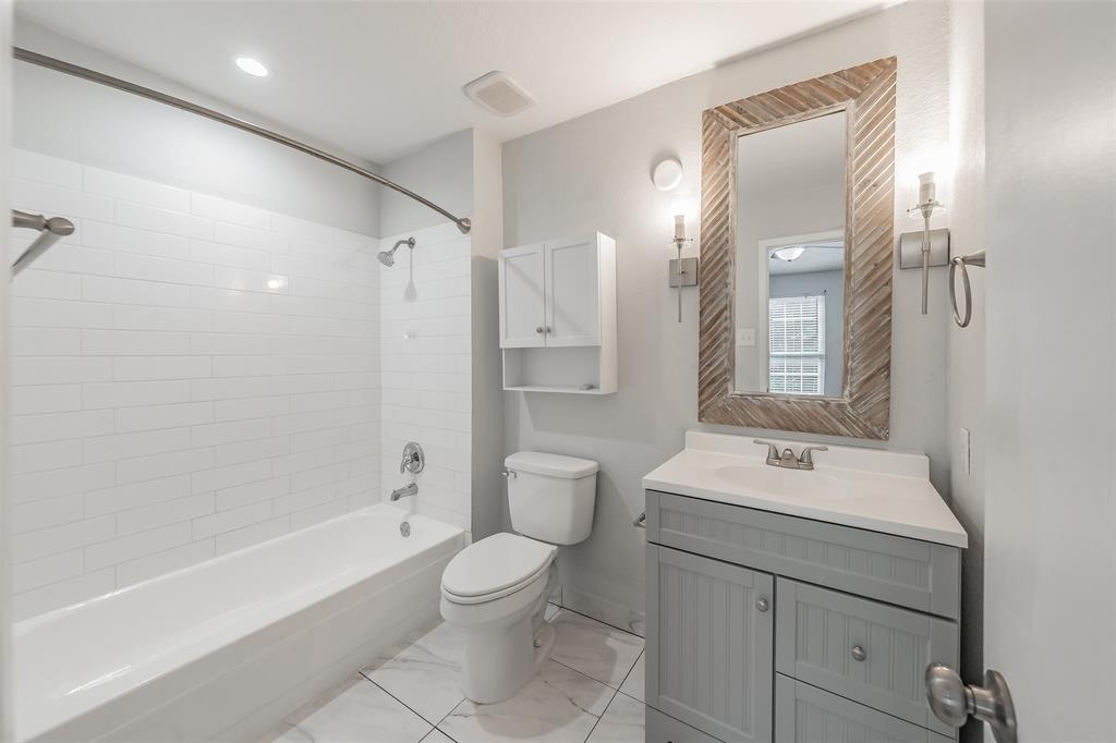 193 Merlin Way Euless, TX 76039 - Photo 21 of 35 Bathroom featuring a white subway tile shower surround, a light gray vanity with white countertop, a decorative wood-frame mirror, and updated lighting