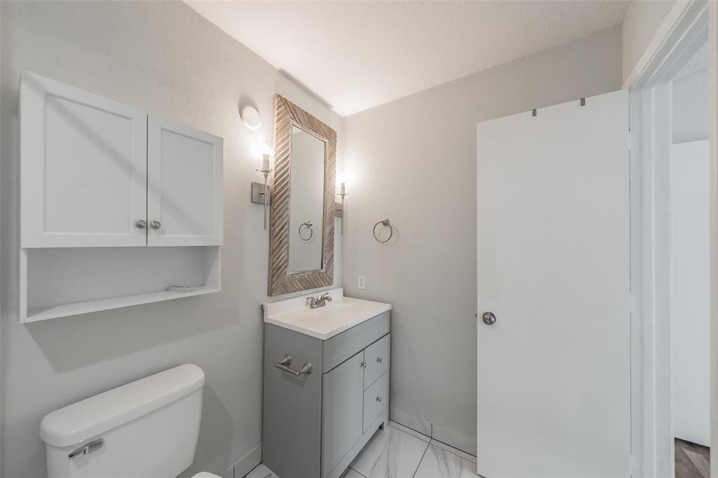 193 Merlin Way Euless, TX 76039 - Photo 22 of 35 Bathroom featuring a gray vanity with integrated sink, a framed wall mirror, sconce lighting, white wall-mounted cabinetry, and tile flooring