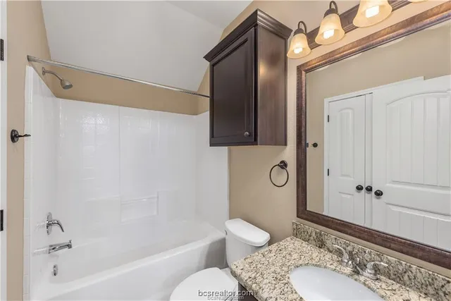 a bathroom with a granite countertop bathtub shower sink vanity and toilet