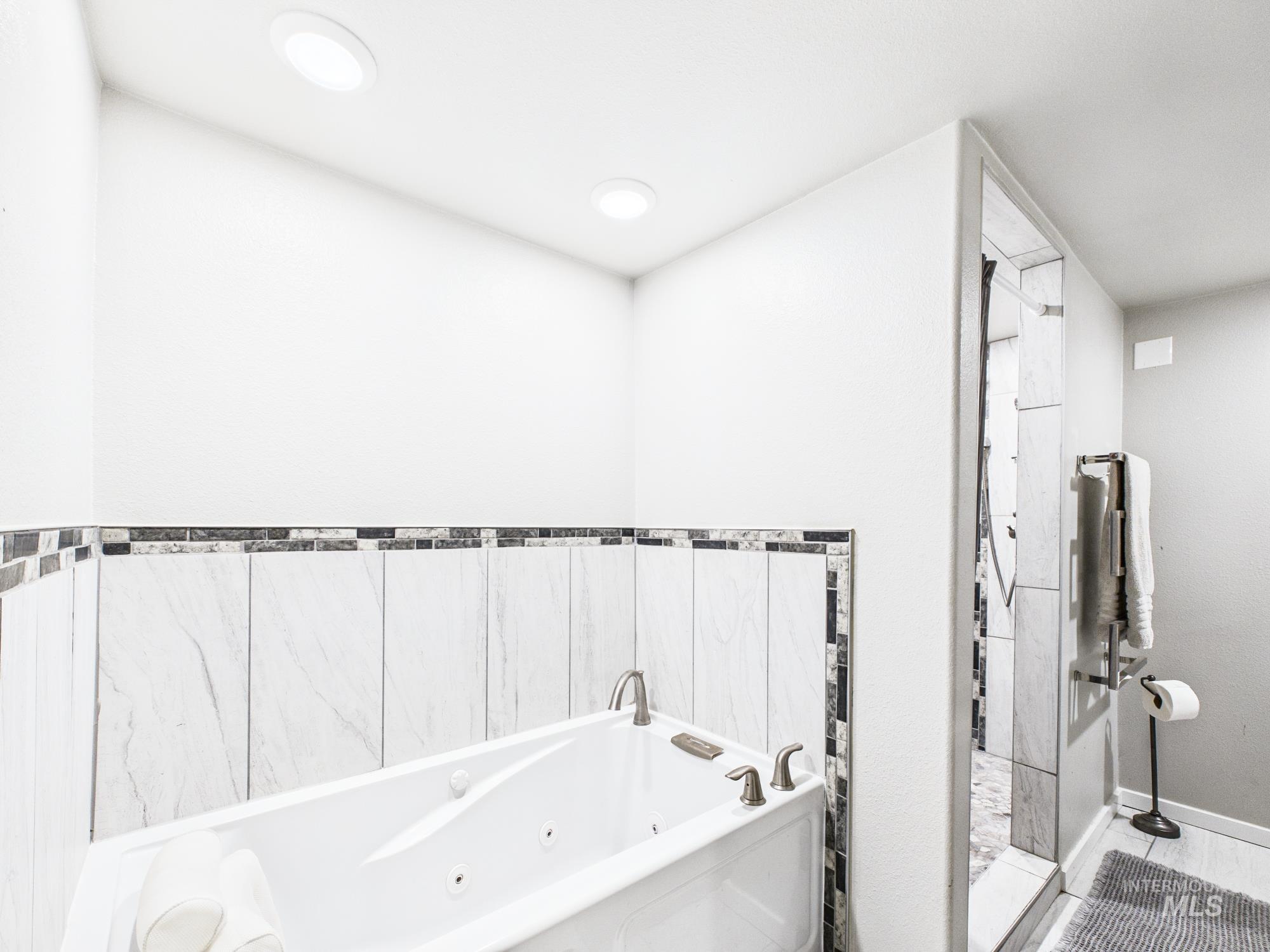 3422 6th Street Lewiston, ID 83501 - Photo 25 of 43 Soaking tub with brushed nickel fixtures, surrounded by white rectangular wall tiles with a decorative mosaic border