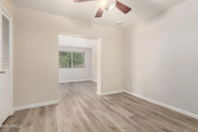 an empty room with wooden floor chandelier fan and windows