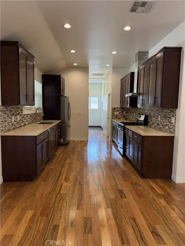 a view of kitchen with stainless steel appliances wooden floor wooden cabinets and a sink