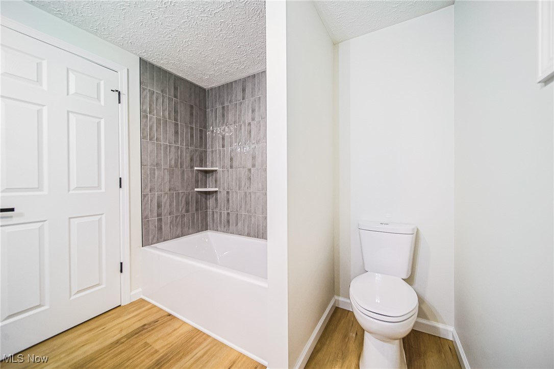 55 Elm Street Rittman, OH 44270 - Photo 22 of 46 Bathroom with wood finished floors, a textured ceiling, toilet, shower combination, and baseboards