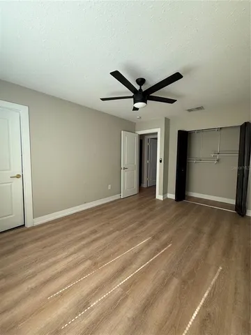a view of an empty room with wooden floor and a ceiling fan